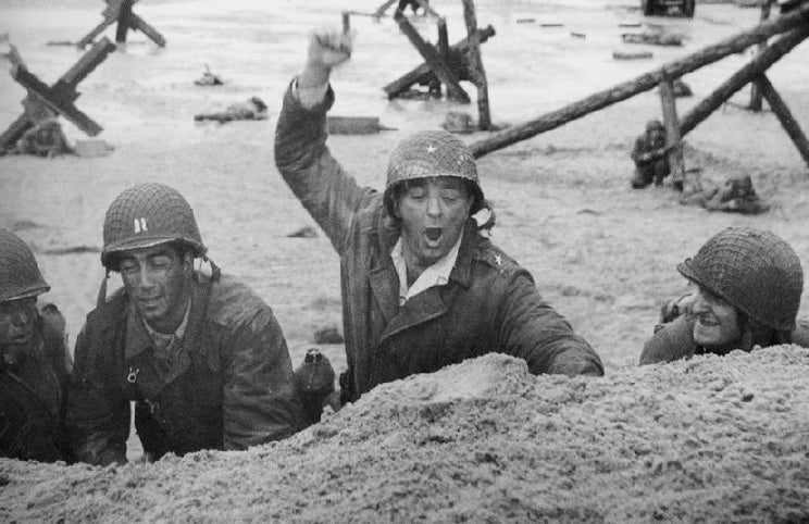 Robert Mitchum (de braço levantado) — recriando a iconografia do desembarque na Normandia