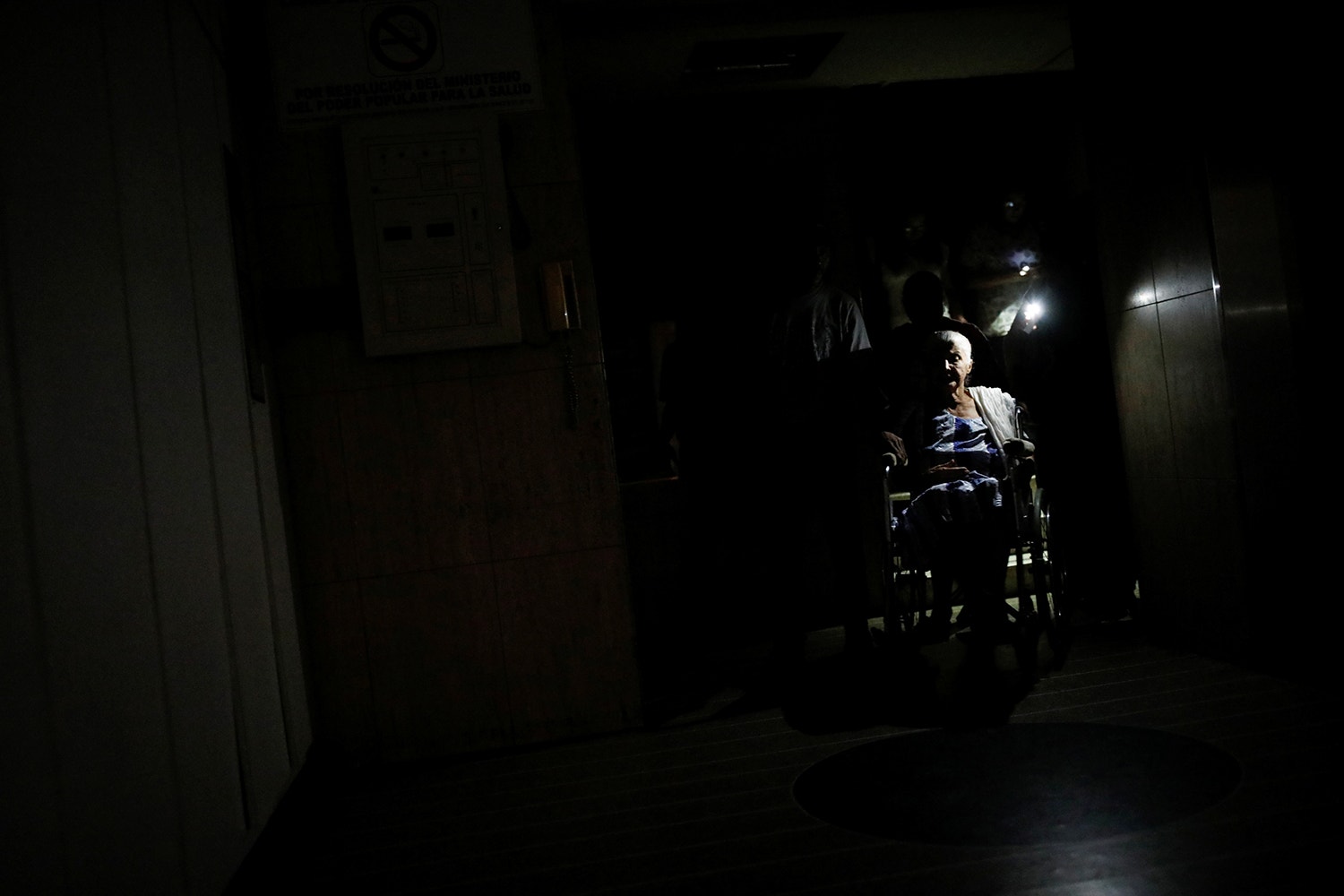  A luz proveniente de telem&oacute;veis &eacute; usada para ajudar Olimpia Mora, que est&aacute; numa cadeira de rodas, a sair de casa em Caracas /Foto: Carlos Garcia Rawlins - Reuters 