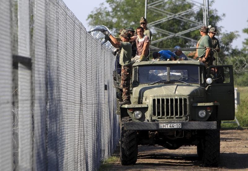 Soldados húngaros completam com rolos de arame farpado a barreira erguida ao longo da fronteira com a Sérvia desde maio de 2015 - Foto: Reuters Soldados húngaros completam com rolos de arame farpado a barreira erguida ao longo da fronteira com a Sérvia desde maio de 2015 - Foto: Reuters