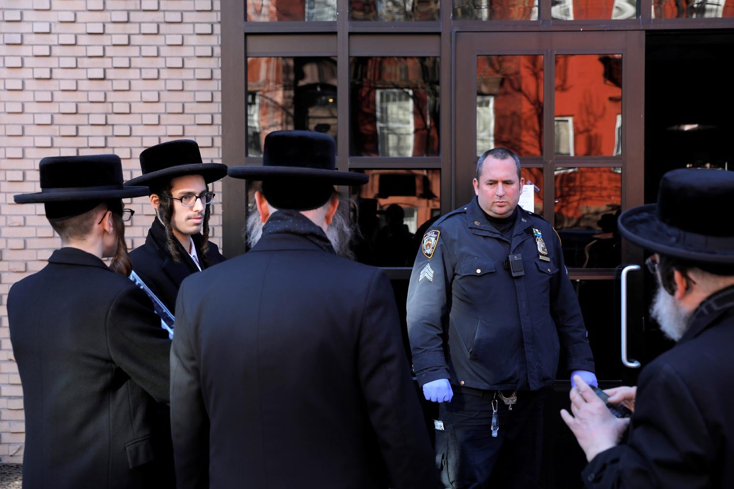 Judeus ortodoxos hass&iacute;dicos frente &agrave; porta de uma sinagoga, encerrada devido &agrave; pandemia de Covid-19 e vigiada por um pol&iacute;cia de Nova Iorque a 18 de mar&ccedil;o de 2020 Foto: Reuters