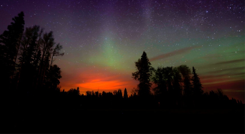  As chamas reluzem por baixo das Luzes do Norte, um fen&oacute;meno tamb&eacute;m conhecido como Aurora Boreal.  