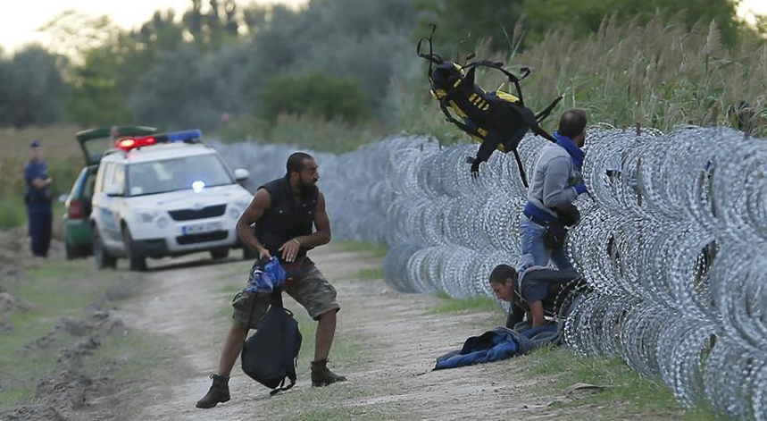 Polícia olha enquanto alguns migrantes entram na Hungria passando por baixo da barreira já erguida nos últimos meses
