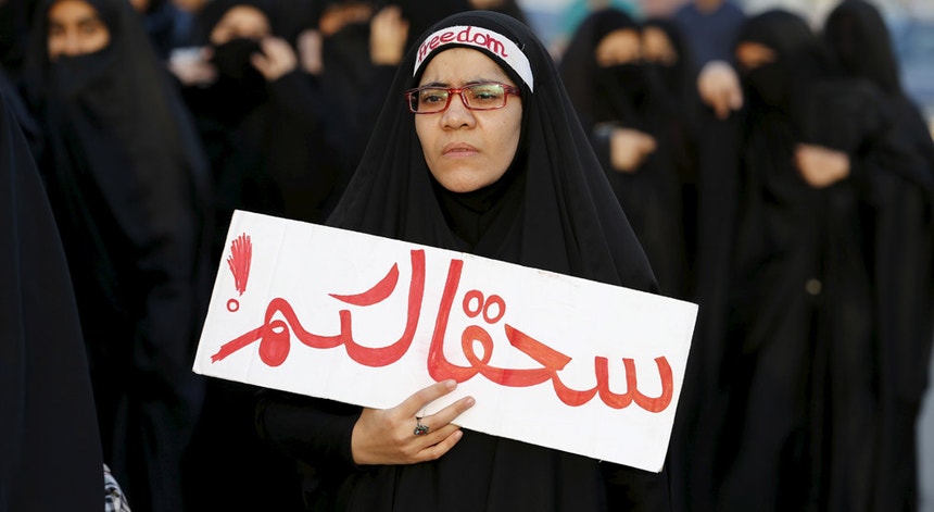 Uma manifestante xiita participa num protesto no Bahrein contra a execução do clérigo Nimr al-Nimr na Arábia Saudita; segura um cartaz com as palavras "vão para o inferno"
