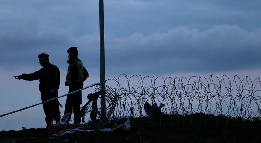 Guardas fronteiriços húngaros de vigilância a migrantes que aguardam vez de passar a fronteira em Botovo, Croácia, a 16 de outubro de 2015. A Hungria anunciou o encerramento das suas fronteiras com a Croácia a partir das 00h00 de sábado, dia 17.
