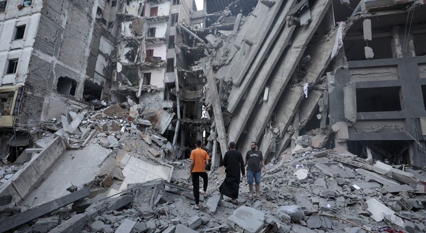 Palestinianos fotografados nas imediações do edifício do Banco Nacional, em Gaza, destruído pelos bombardeamentos aéreos israelitas
