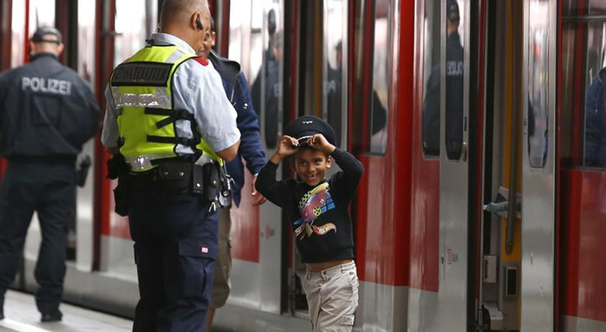 Um rapazinho migrante brinca com o chapéu de serviço de um polícia austríaco durante a transferência de comboios que o irá levar de Salzburgo, na Áustria, aos arredores de Munique, Alemanha.
