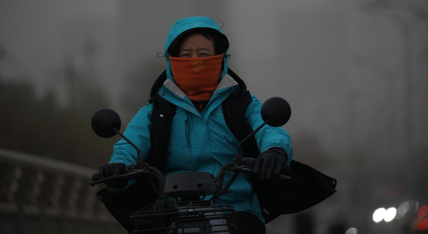 Uma habitante de Pequim arriscou sair à rua e circular dia 16 de abril de 2021, apesar dos avisos quanto a mais uma tempestade de poeira em cinco semanas
