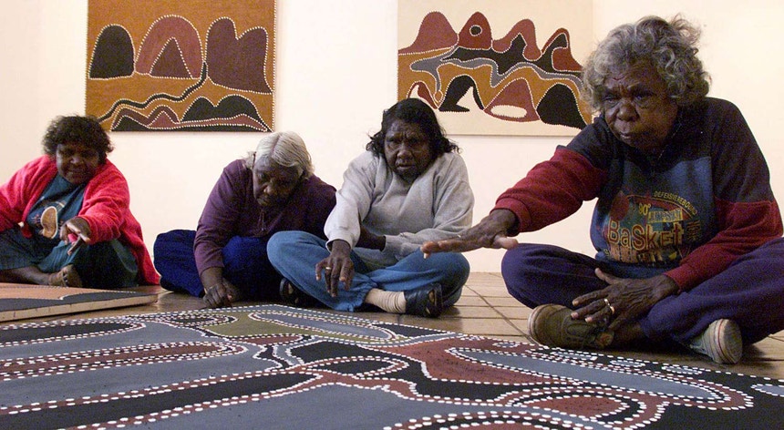 Grupo de mulheres aborígenes, sentadas em frente de obras de pintura
