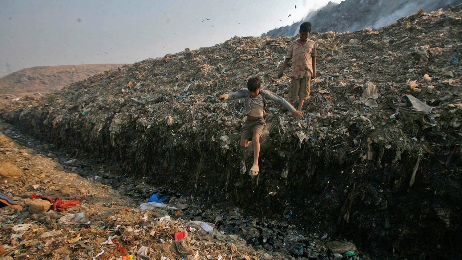  Dinesh Mukherjee de 11 anos, cujo trabalho &eacute; recolher lixo,  observa o seu amigo a saltar para uma po&ccedil;a de lixo t&oacute;xico no aterro de Ghazipur, em Nova Deli. 10 de novembro de 2011. | Parivartan Sharma - Reuters 