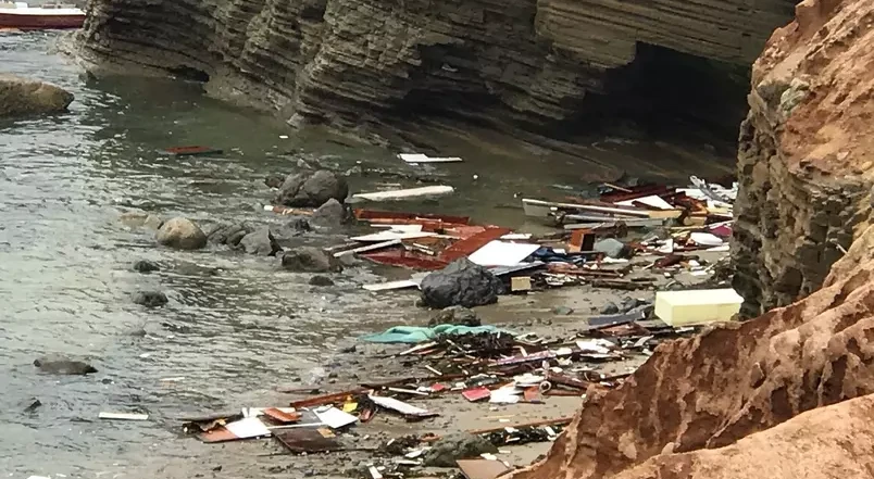 Os destroços da embarcação junto à costa
