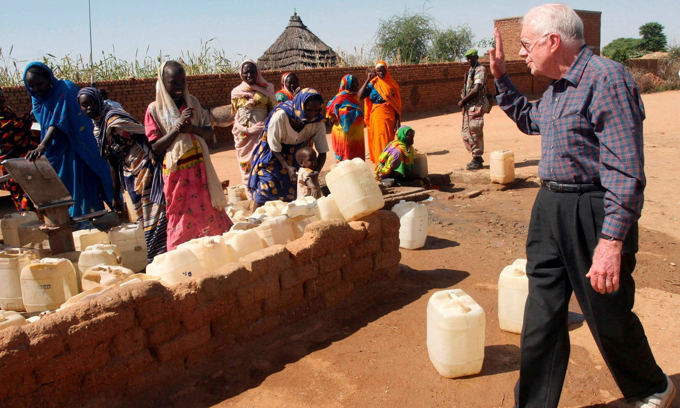  Jimmy Carter, do Grupo de Anci&atilde;os, acena para mulheres deslocadas internamente num ponto de abastecimento de &aacute;gua na cidade de Kebkabiya, no norte de Darfur, Sud&atilde;o, 3 de outubro de 2007 | Mohamed Nureldin Abdalla - Reuters 