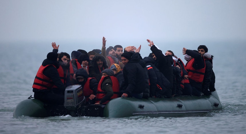 Migrantes acenam a bordo de um barco antes de tentar a travessia do canal da Mancha
