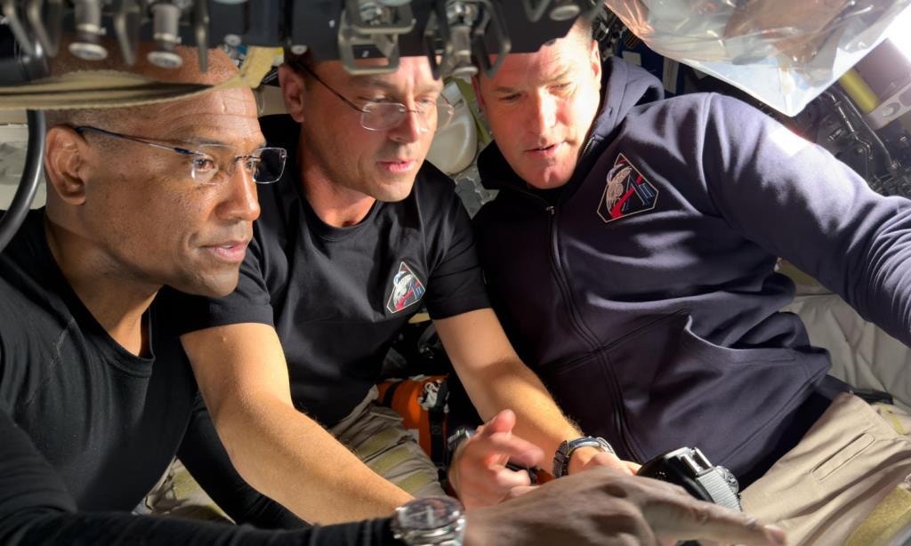  Miss&atilde;o Artemis II, dia 6. O piloto da Artemis II, Victor Glover, o comandante Reid Wiseman e o especialista de miss&atilde;o Jeremy Hansen preparam-se para a jornada ao redor do lado oculto da Lua, configurando seus equipamentos de c&acirc;mara pouco antes de iniciarem suas observa&ccedil;&otilde;es de sobrevoo lunar. Cr&eacute;dito da imagem: NASA 