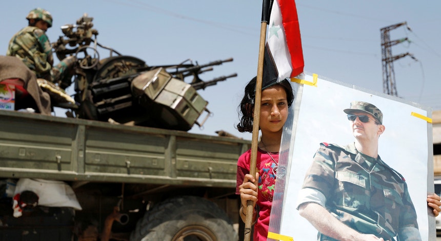 Uma rapariga segura uma bandeira síria e uma fotografia de Bashar al-Assad em Deraa
