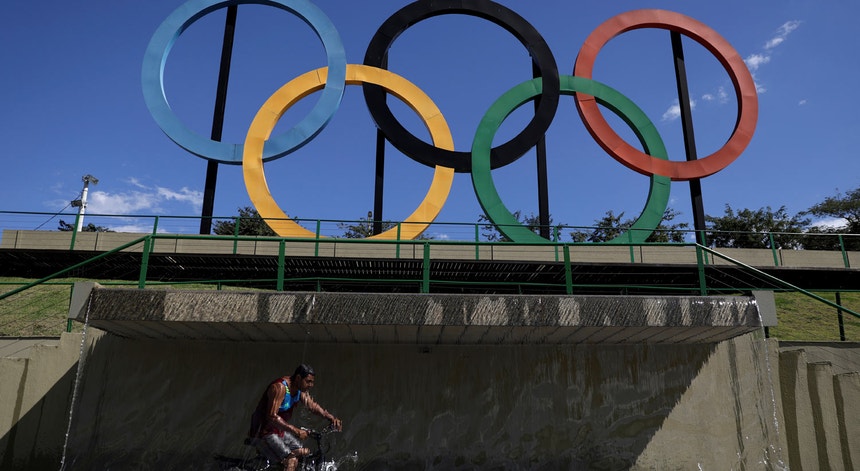 Um rapaz passa de bicicleta numa cascata sob o símbolo olímpico num estádio do Rio de Janeiro
