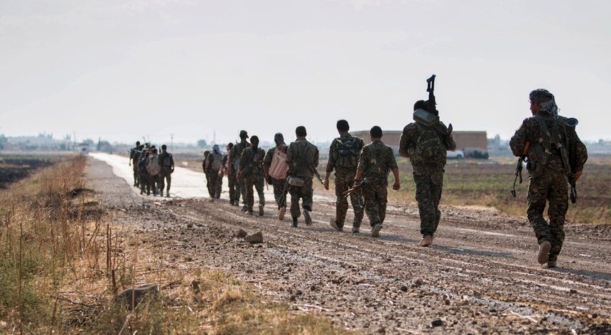 Forças armadas curdas das Unidades de Proteção Popular caminham estrada fora perto de Tel Abyad no governorato de Raqqa, após garantirem o controlo da zona em junho de 2015
