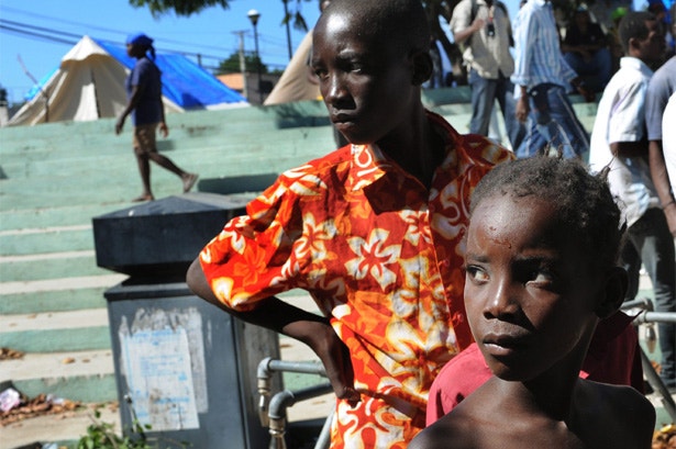  Dois jovens haitianos aguardam a sua vez para beber um pouco de &aacute;gua pot&aacute;vel de um cano instalado num campo de deslocados 
