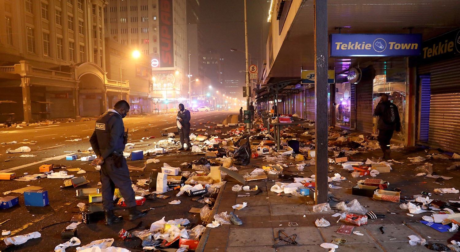  Os agentes da pol&iacute;cia olham para os restos de lojas saqueadas no centro de Durban | Foto: EPA 