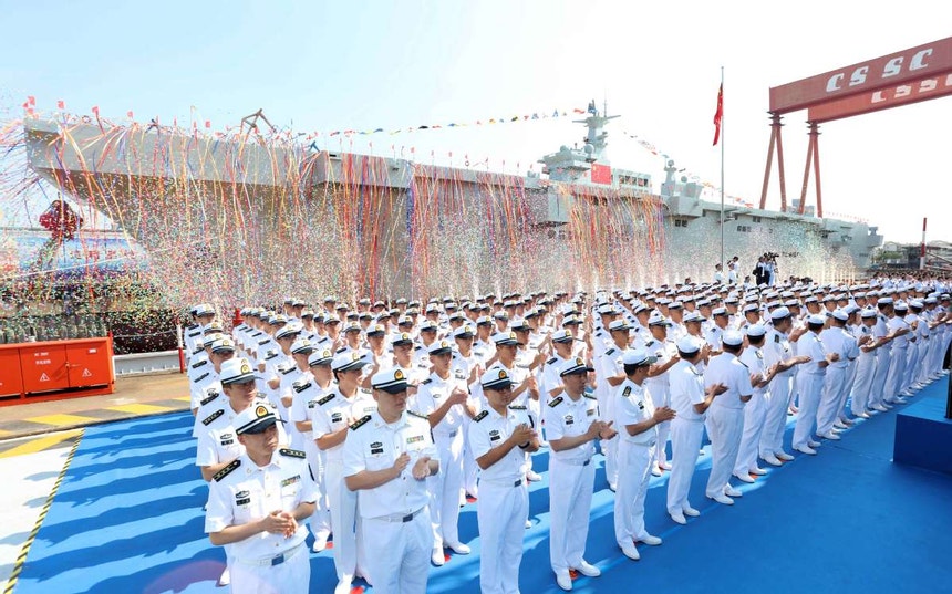 Imagem relacionada com a notícia: Oficiais da Marinha do Exército de Libertação Popular chinês participam da cerimónia de lançamento do primeiro navio de assalto anfíbio,em Xangai
