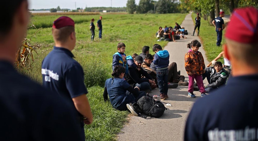 A polícia húngara de guarda a um grupo de migrantes que tentou passar a vedação fronteiriça durante a noite.  Pelo menos 16 pessoas foram detidas após o reforço da segurança da fronteira húngara e devido às novas leis anti-imigração que entraram em vigor à meia-noite.
